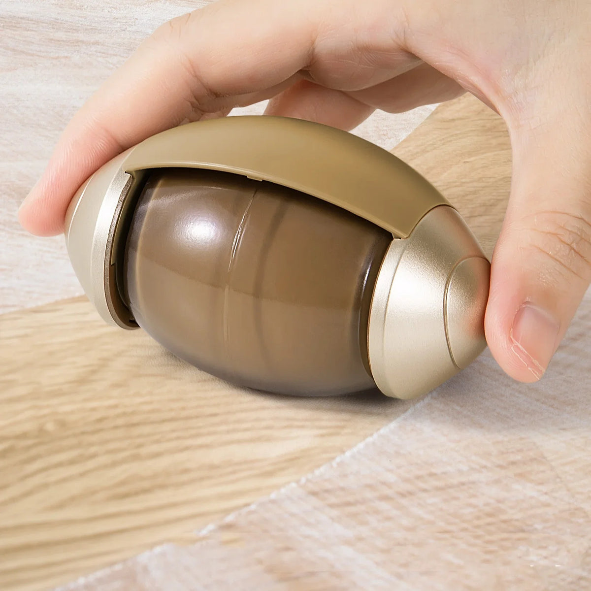 Hand holding sleek gold pet hair remover on wood floor, ideal for fur-free living